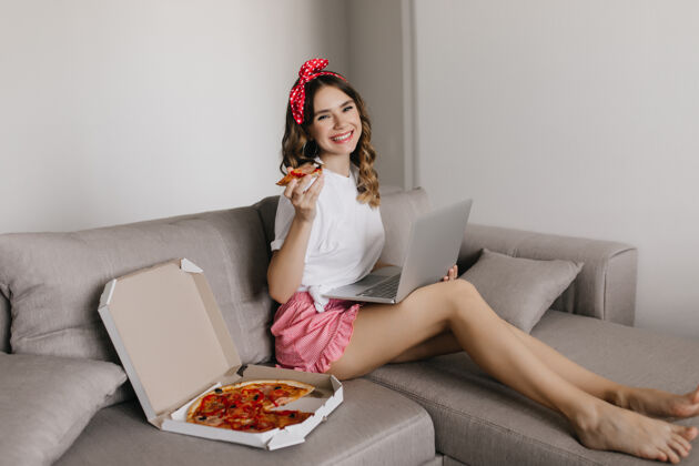 成人光脚优雅的女孩看电影和吃比萨饼室内拍摄微笑的女自由职业者使用笔记本电脑和享受意大利美食室内Wifi房间