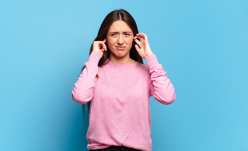 魅力年轻漂亮随意的女人看起来生气 压力和烦恼 捂着双耳听震耳欲聋的噪音 声音或大声的音乐头发肖像漂亮