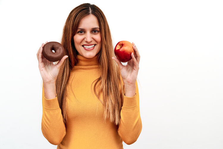 保健一只手拿着甜甜圈 另一只手拿着苹果 一个面目全非的女人在怀疑吃什么饮食营养坏