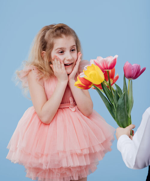 儿子穿粉红色衣服的小女孩收到鲜花 隔离在蓝色的墙上 特写 两个小孩奇迹惊人童年