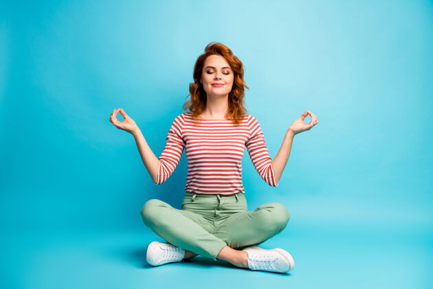 快乐安静安详女士的全尺寸照片坐在地板上交叉双腿展示om标志运动瑜伽冥想穿着时尚的绿色套装隔离蓝色瑜伽腿灵感
