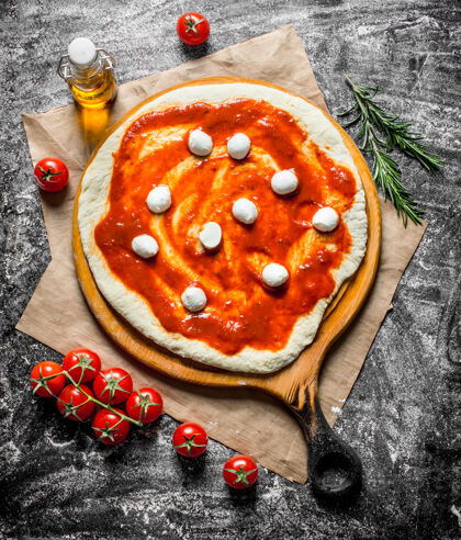 小麦生披萨用意大利干酪和番茄酱在乡下的桌子上擀面团切割迷迭香圆形