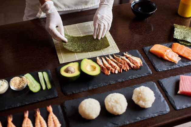 鲑鱼制作卷寿司过程的特写镜头厨师的手拿着一张诺丽配料：黄瓜 三文鱼 米饭 鳄梨放在黑石板上厨师鳗鱼过程