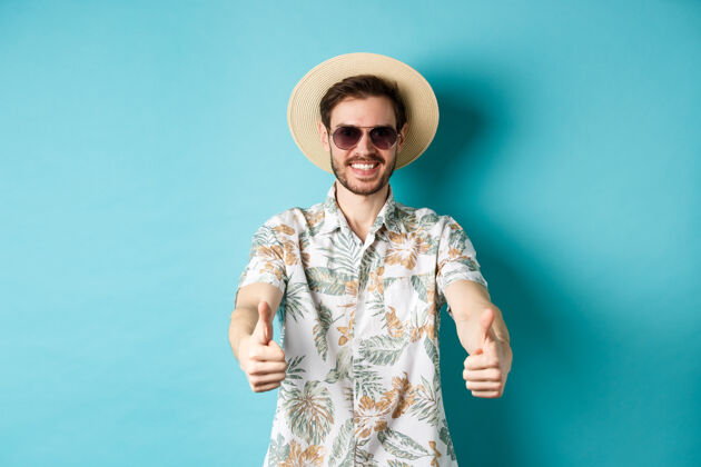 朋友戴着墨镜 戴着草帽 竖起大拇指 微笑着 站在白色的背景上 享受着暑假的快乐休闲成人自信