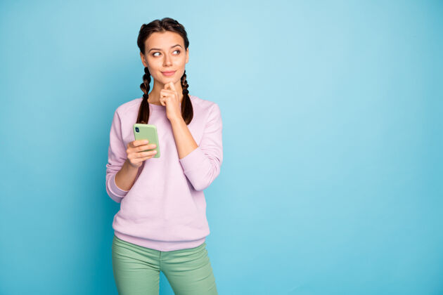 影响者美女手持电话的照片现代用户思考新博客创意广告文字穿休闲时尚粉色毛衣绿色裤子隔离蓝色女人信息思考