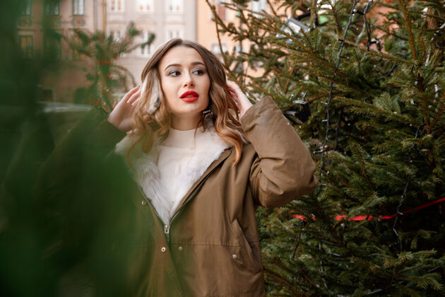 年轻穿着针织毛衣和蓬松耳机的白人女士户外写真年轻美丽快乐的微笑女孩穿着皮草外套在装饰圣诞树附近波兰情感雪花时尚