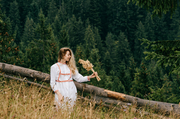 自然年轻迷人的金发女孩在白色礼服与刺绣摆姿势与小穗花束在风景如画的景观姿势乡村刺绣