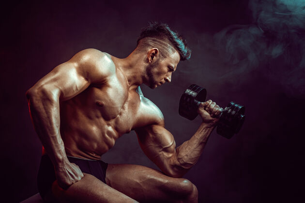 举重运动员在工作室里用烟在黑暗的墙上锻炼肌肉强壮的健美运动员拥有完美的腹肌重重量赤膊