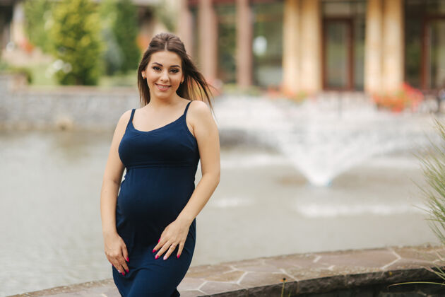 女人美丽的年轻开朗的孕妇站在喷泉的背景下女性怀孕公园