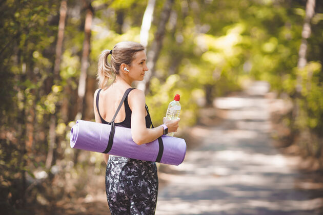 持有一个穿着运动服的女人 运动后拿着瑜伽垫和水瓶减肥健美操女孩