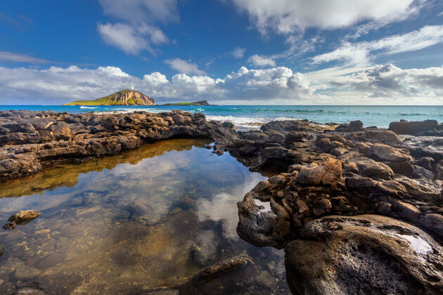 休息靠近马卡普海滩的岩石 背景是马纳纳和高希开普群岛白天海岸岛屿