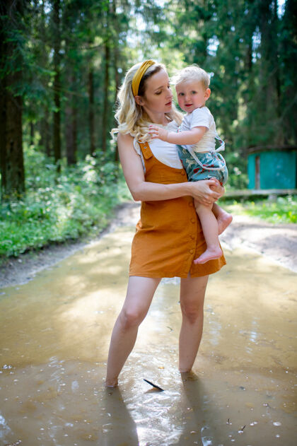 森林年轻的母亲抱着儿子站在森林的水坑里蹒跚学步搞笑家庭