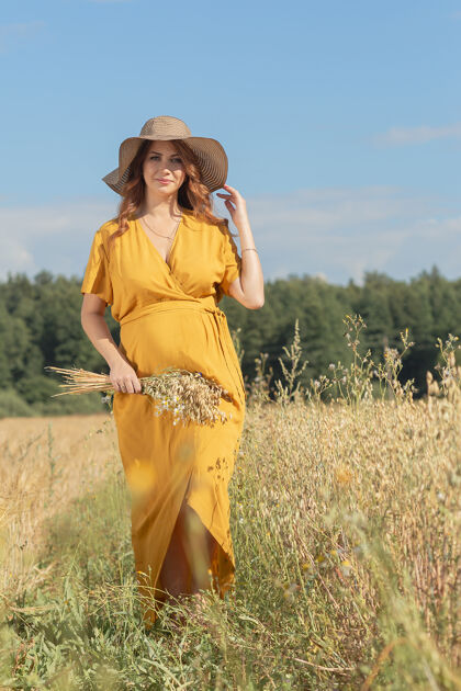 肚子在一个阳光明媚的夏日 一位年轻漂亮的孕妇穿着黄色的裙子 戴着黄色的帽子 走过一片麦田婴儿麦田欢呼