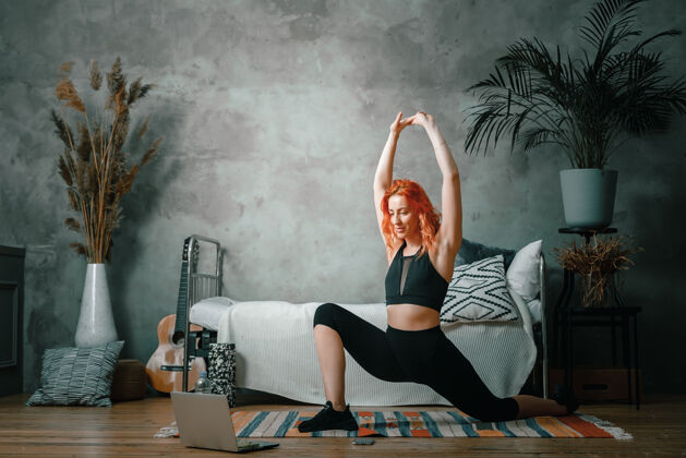 女性一个年轻女子在家里参加体育活动 通过笔记本电脑在线锻炼运动哑铃身体