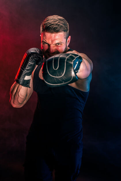 踢留着胡须 纹身的泰拳运动员 身穿黑色汗衫 戴着拳击手套 在黑暗的墙上与烟雾搏斗运动概念攻击性准备男性