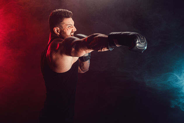 男子留着胡须 纹身的泰拳运动员 身穿黑色汗衫 戴着拳击手套 在黑暗的墙上与烟雾搏斗运动概念男性战斗拳击手
