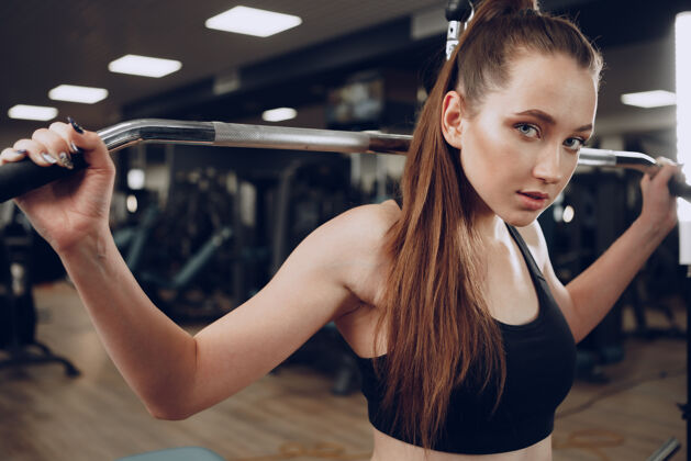 健身迷人的年轻女子在健身房锻炼手臂和背部的肌肉运动员健身房运动服
