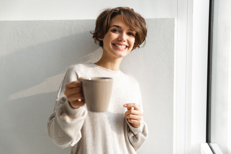 室内微笑的年轻女子早上在厨房喝茶举行咖啡馆咖啡
