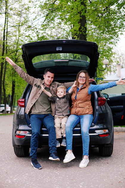 越野幸福的夫妇和他们的小儿子在开放的越野车后备箱在停车场停车儿子户外