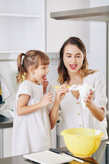 积极的情绪在家做生日蛋糕时 兴奋的小女孩看着妈妈往糕点袋里装奶油食物准备烹饪兴奋