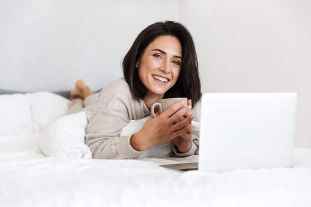 床一张30多岁的中年妇女在明亮的房间里躺在床上用笔记本电脑的照片可爱成熟白种人