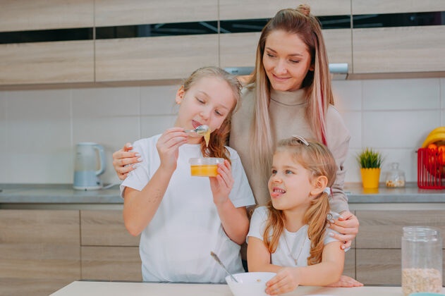 家庭一位母亲和她的两个女儿在厨房里给燕麦片加蜂蜜早餐爱碗