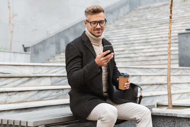 帅哥帅哥穿着夹克拿着手机 坐在户外喝外卖咖啡秋天白种人咖啡