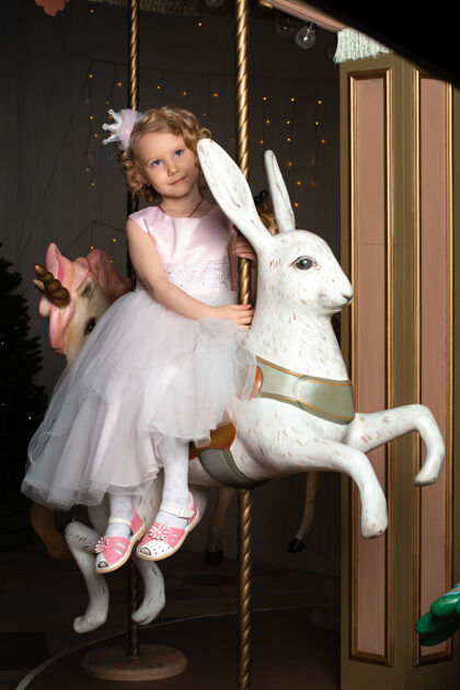 女儿一个穿着粉色裙子戴着皇冠的小女孩和一只白兔坐在旋转木马上房间新的小