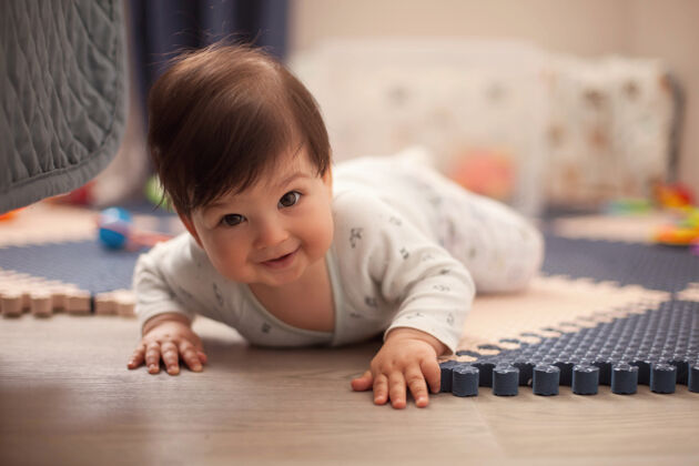 天真穿着明亮的睡衣 一头黑发的漂亮男婴正在学习爬行 趴在托儿所的地板上婴儿床床呆着