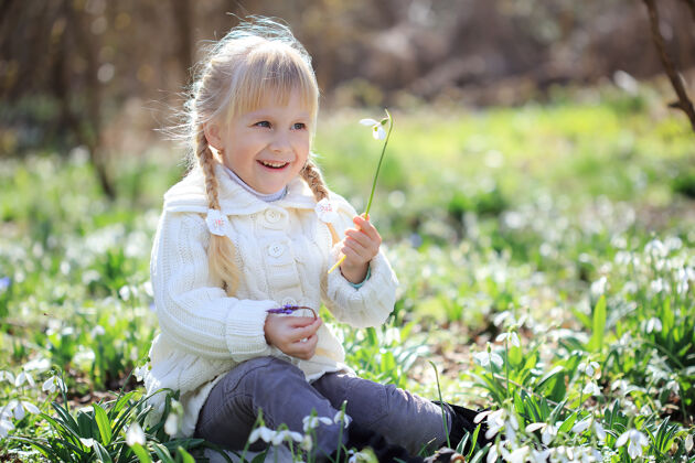 夏天一个漂亮的女孩正坐在一片鲜花盛开的草地上穿着白色针织毛衣的漂亮小女孩在春天的森林里散步复活节时间四月太阳快乐