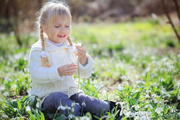 田野一个漂亮的小女孩正坐在一片鲜花盛开的草地上一个穿着白色针织毛衣的小女孩正在考虑放雪球复活节时间春天阳光明媚的森林采摘森林传统