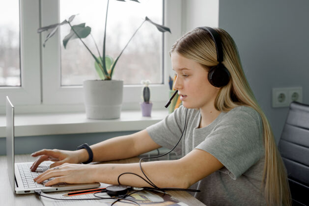 计算机戴着耳机微笑的少女在家里上网络课远程设备笔记本电脑