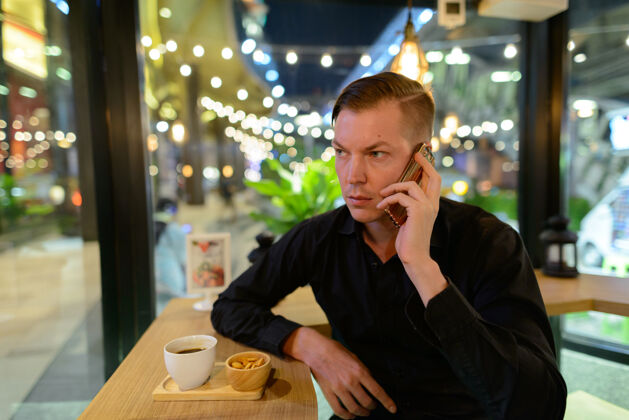 现代年轻英俊的斯堪的纳维亚商人在咖啡店放松的画像手机坐着咖啡
