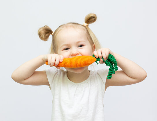 白色小女孩正在吃白色背景上的玩具胡萝卜健康食品小欢呼饮食