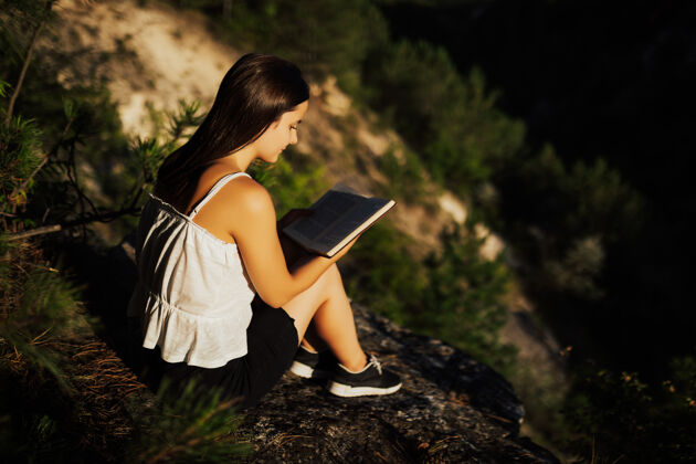 生活方式年轻的女孩在看书 而坐在美丽的自然风景享受天农作物