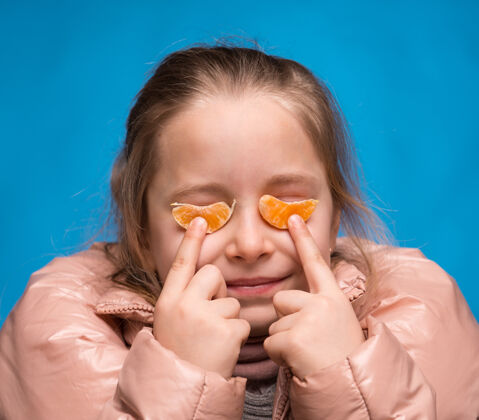 多汁蓝色背景上戴着橘子眼镜的女孩脸维生素柑橘
