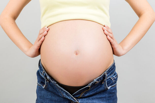 身体一个穿着无拉链牛仔裤的孕妇露出了她裸露的腹部婴儿怀孕碰撞