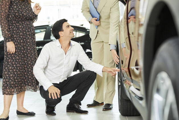 客户年轻人一边检查新车的轮子 一边和女士参观汽车展厅 一边和经理交谈男人经理购买