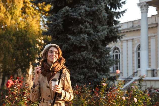 成人可爱的年轻女子穿着外套走在户外 喝着咖啡吸引力长相服装