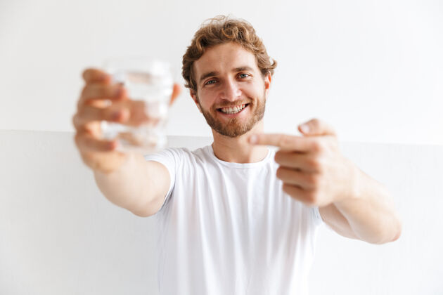 概念微笑的年轻人展示着一杯水 站在家里的墙上手势男人玻璃