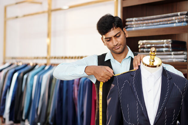零售严肃的印度裁缝正在人体模型上测量定制的西装外套人体模特企业家工业