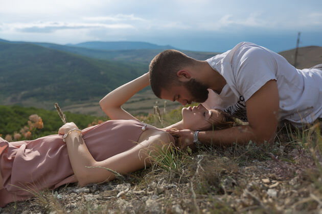两个一对年轻的夫妇 一男一女 躺在草地上 在青山绿水的映衬下互相对视天空美丽自然户外假期风景