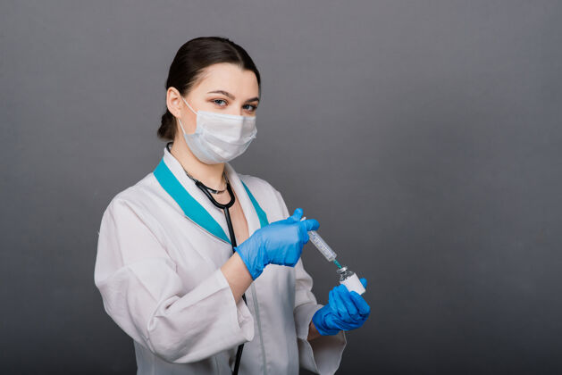 面罩严肃的女医生戴着医用口罩拿着注射器和疫苗隔离在灰色上摄影棚拍摄医院医疗保健
