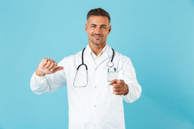 顾问自信的男人医生穿着制服孤立地站在蓝色的墙上 指着自己指点手势医院