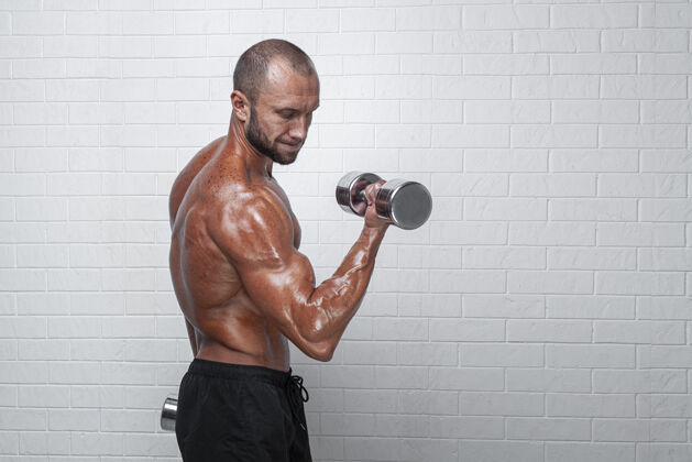 男人健美运动员在砖墙上用哑铃练习二头肌举重男人健身
