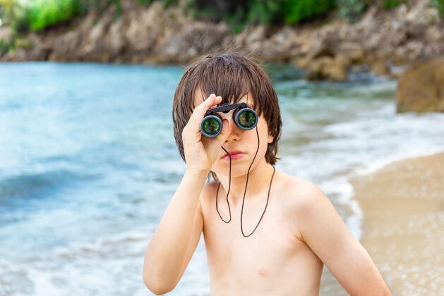 年轻人一个小男孩呆在海边的海滩上 用望远镜看东西年轻人山岩石
