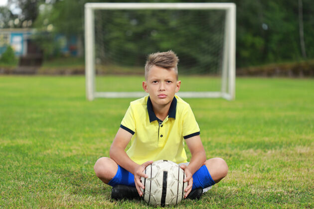 球穿着黄色t恤和蓝色gntra的帅哥足球运动员坐在足球场上男孩领域制服
