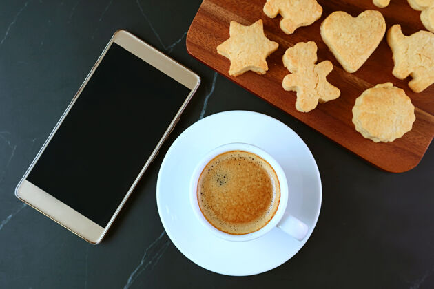 通信一杯热咖啡和一部配有可爱动物形状饼干的白屏智能手机咖啡屏幕刷新