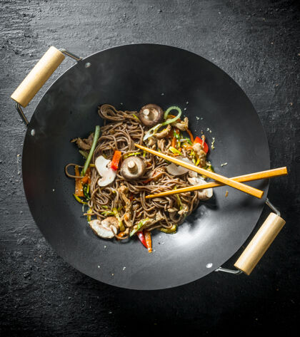 胡椒在黑木桌上用筷子在平底锅里炒面快餐薯条美食