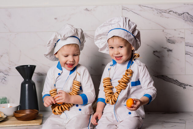 膳食小可爱的厨师拿着餐具坐在厨房里 双胞胎兄弟 橘子 百吉饼营养白人欢呼